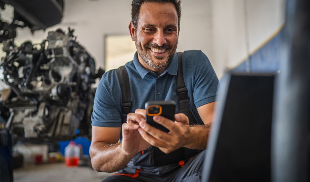 A mechanic in his workshop smiling at a text on his phone